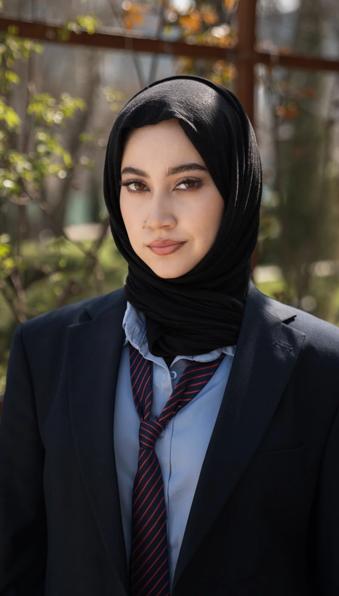 Marifat Jamal, portrait in a dark blazer, light blue shirt and striped tie, outdoors among trees