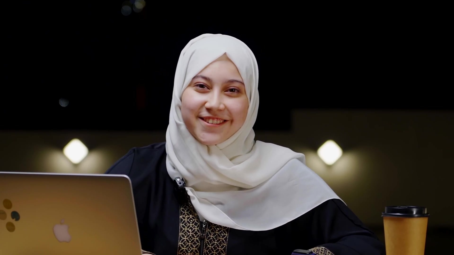 Marifat Jamal smiling at a desk with a laptop, in the setting of her YouTube videos